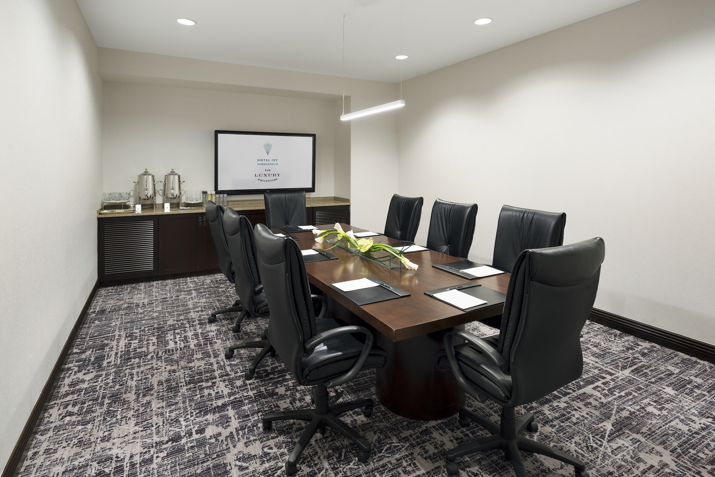 A wooden desk and black leather office chairs with the screen and amenities set up in a meeting venue, Boardroom at Hotel Ivy