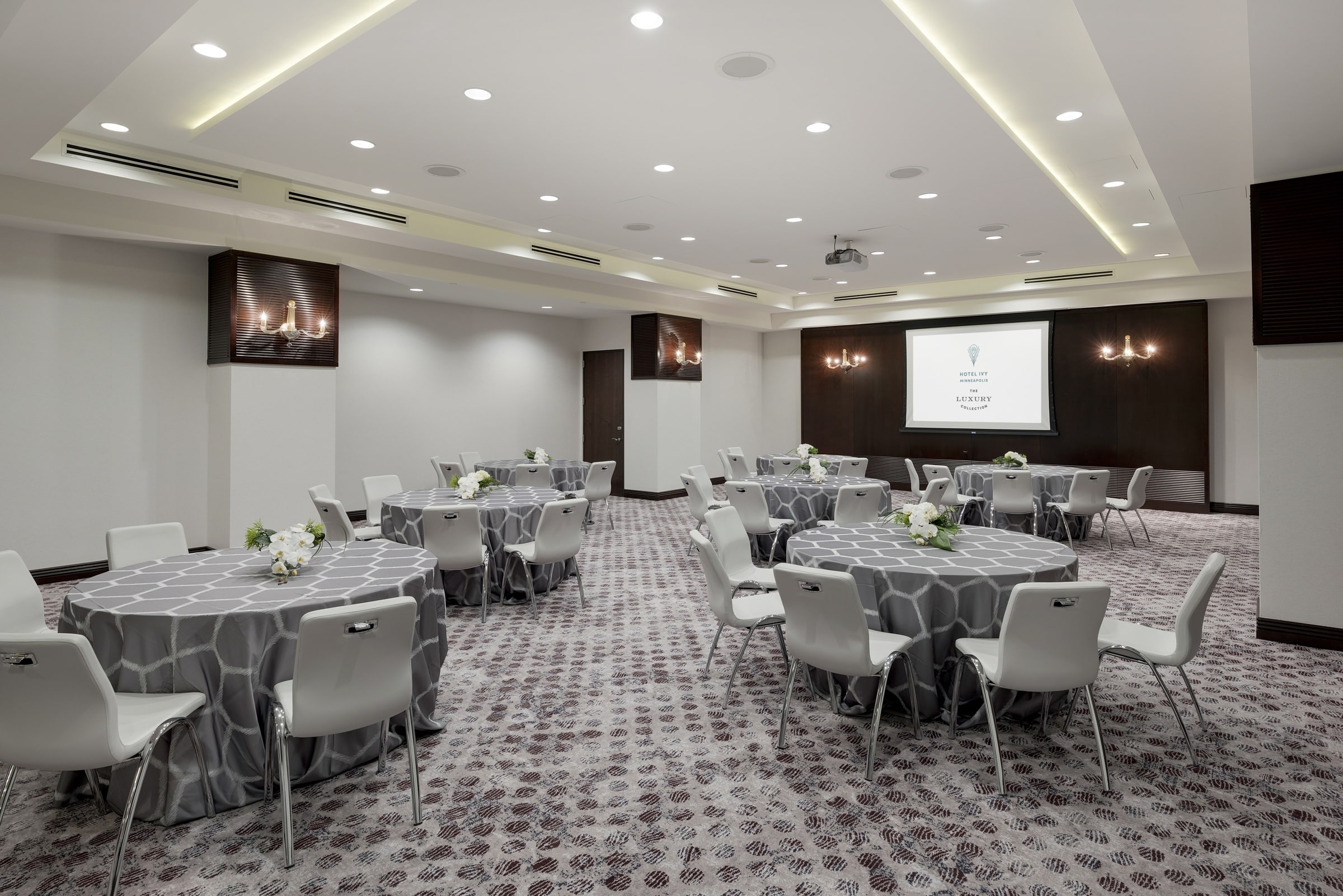 Round tables with grey chairs and a monitor in a large venue, Grand Salon, at Hotel Ivy