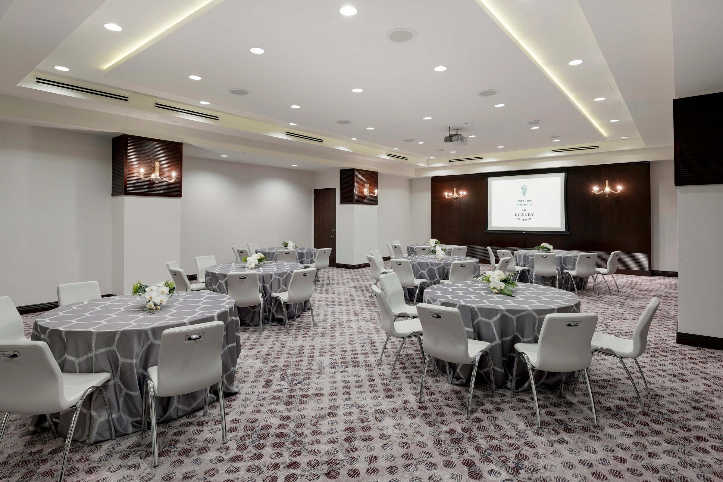 Round tables with grey chairs and a monitor in a large venue, Grand Salon, at Hotel Ivy