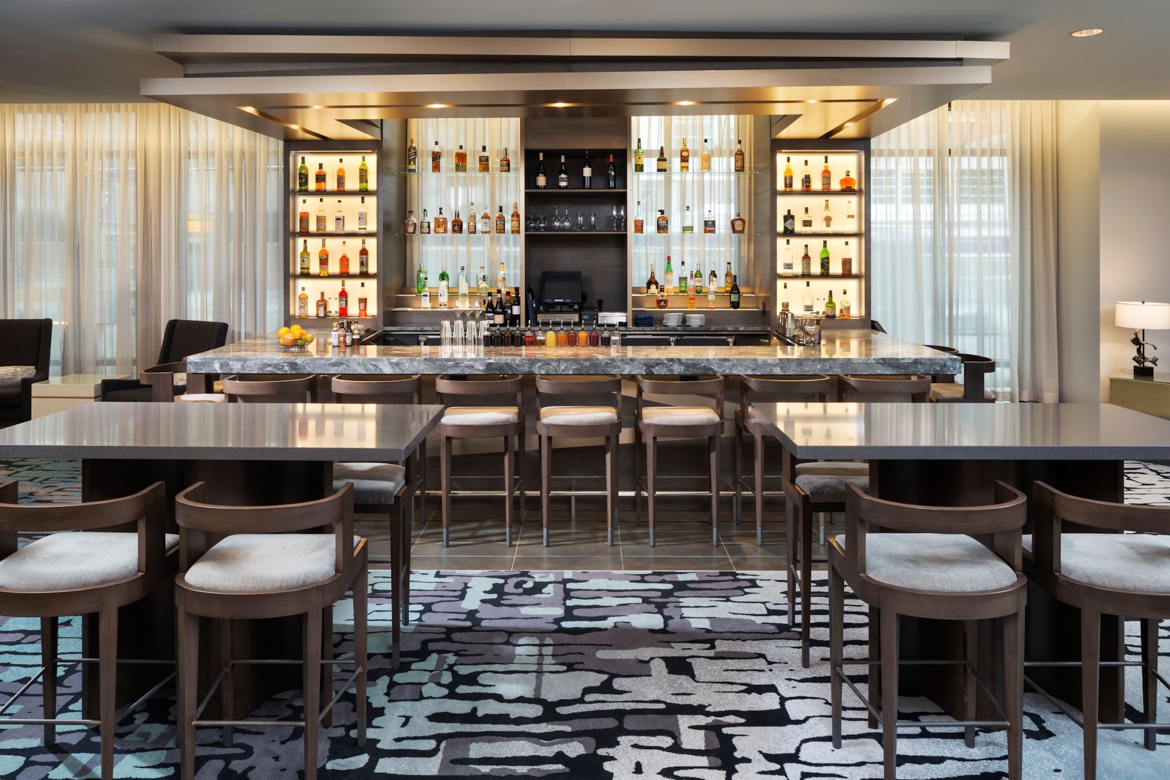 A decent selection of liquor with white curtain, grey marble bar table, grey high table with comfortable chairs at Bar Edera