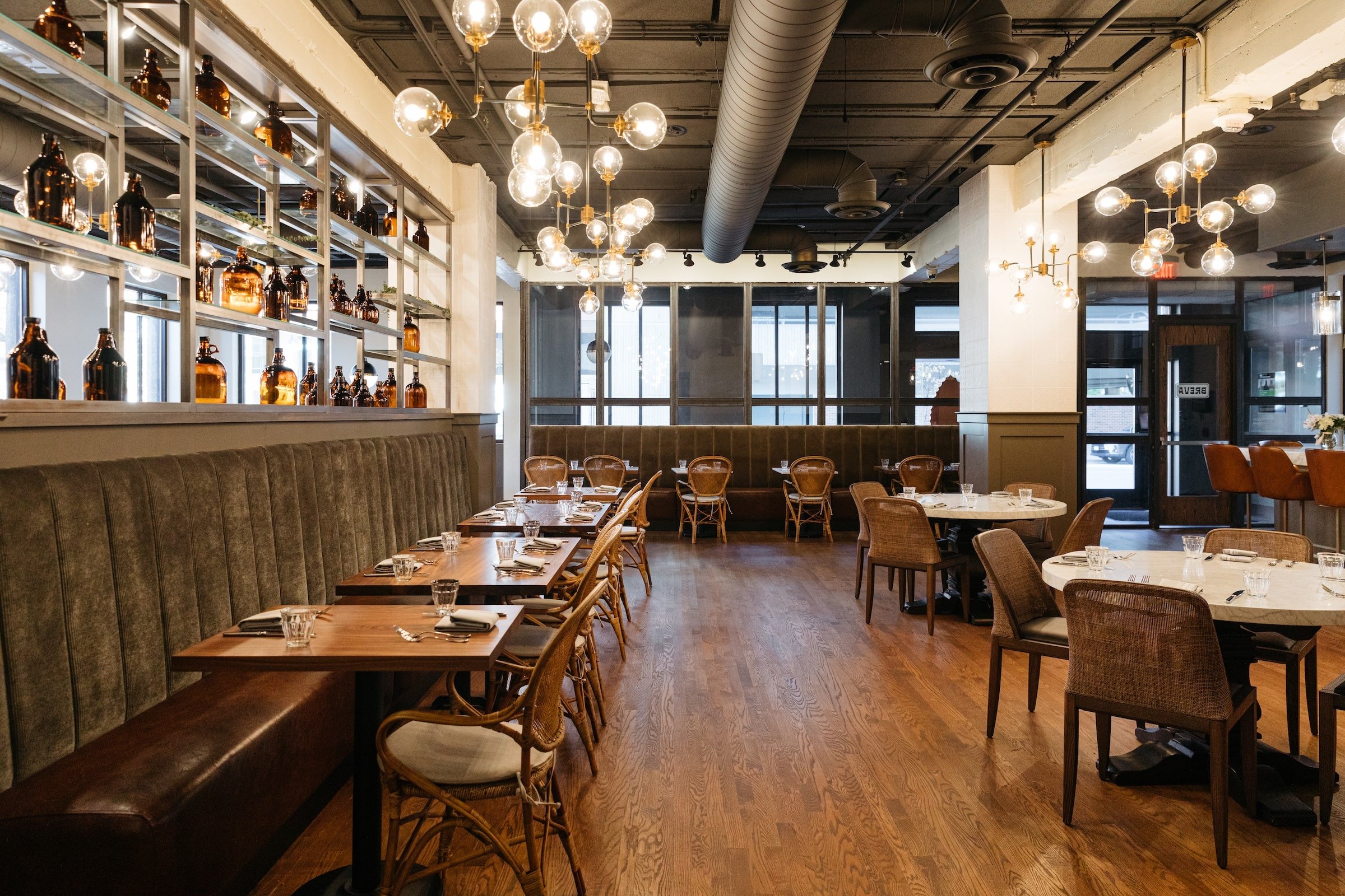 Interior of Breva Bar is & Grill from Hotel Ivy - Dining tables with large glass under round light bulbs in a bright space