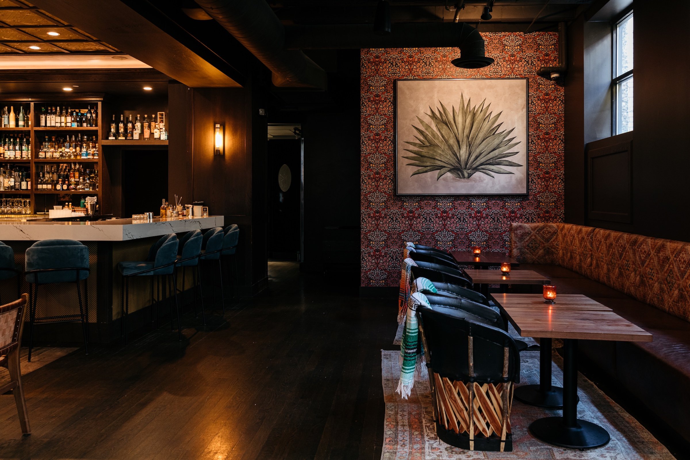 a marble bar table, regular wooden dinning tables, and agave painting on red wall with unique patterns at Masa & Agave