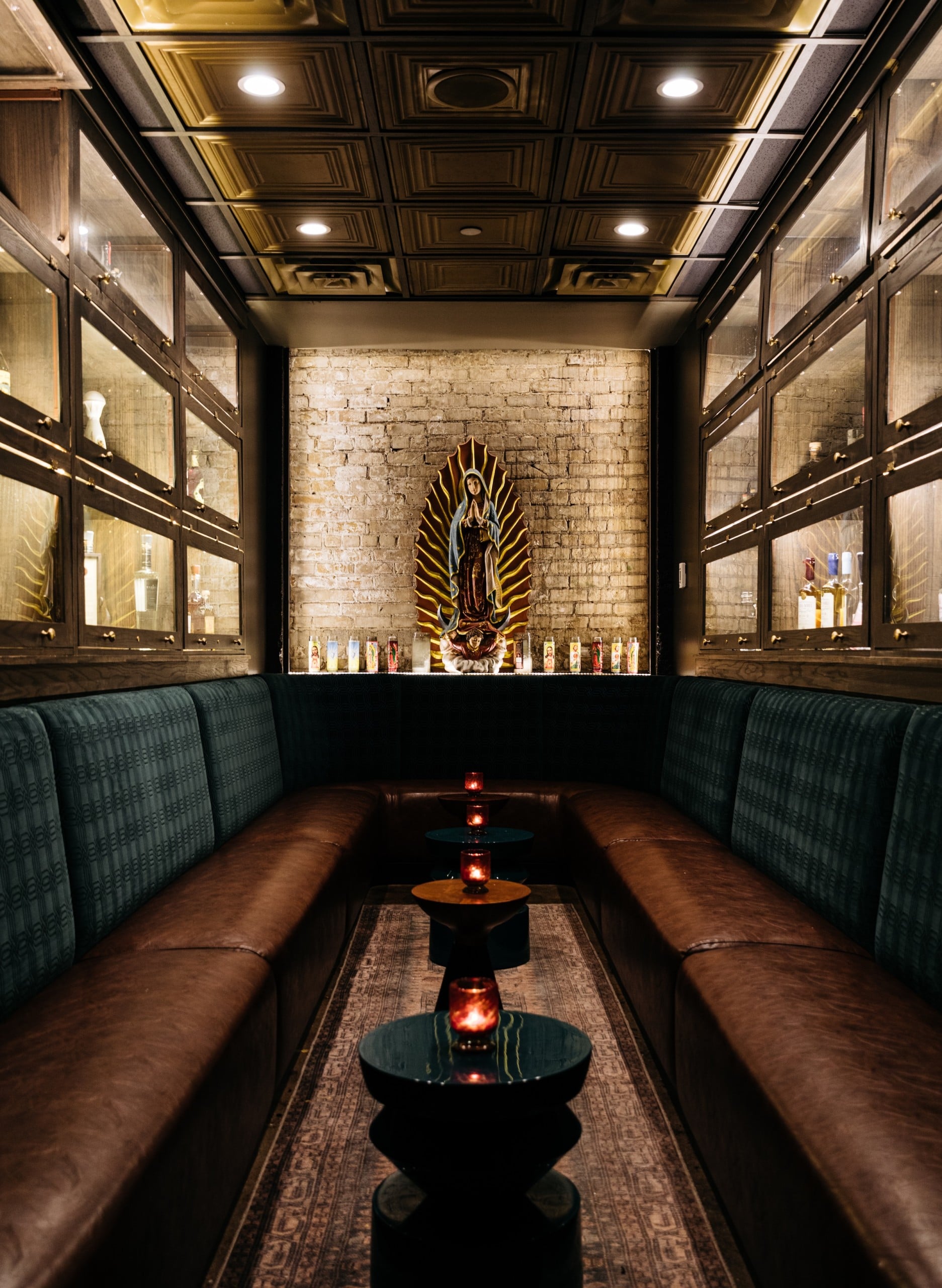 A sacred woman status, U-shaped comfortable couch with small round tables next to Tequila collections in Tequila Chapel from Masa & Agave of Hotel Ivy